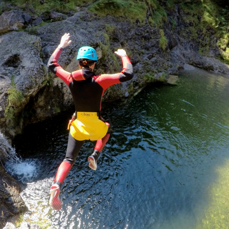 Eine Person springt beim Canyoning in der Starzlachklamm in einen klaren Wasserpool, umgeben von Felsen und Vegetation.