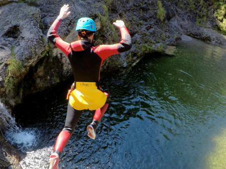 Person springt beim Canyoning in deiner Nähe in einen grünen Fluss in einem felsigen Umfeld, mit Helm und Neoprenanzug.