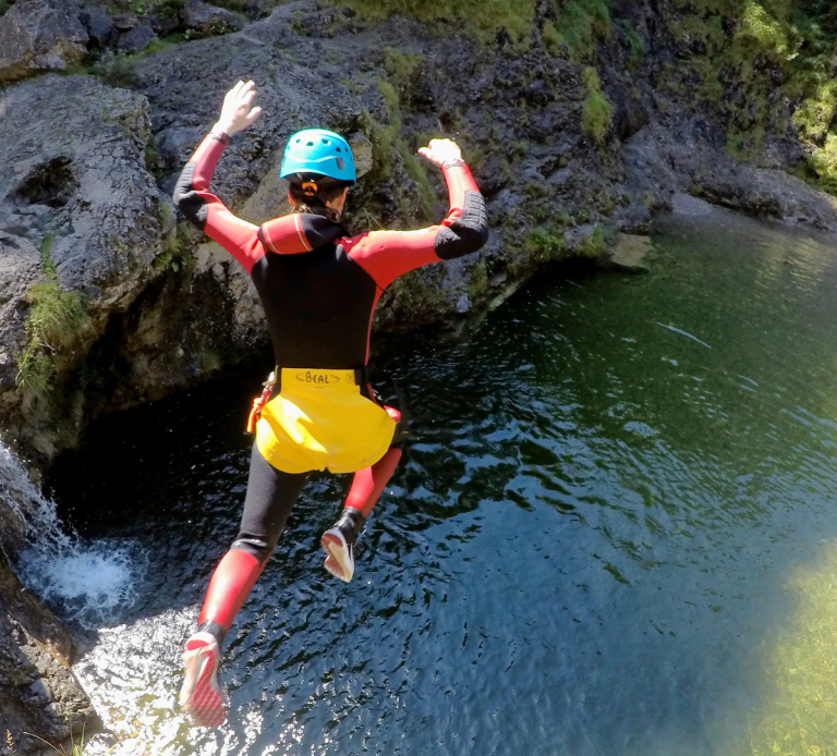 Person beim Canyoning in der Starzlachklamm in Taucheranzug springt von einem Felsen ins klare Wasser.