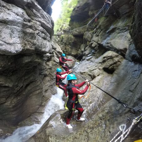 Drei Personen im Neoprenanzug klettern beim Canyoning in der Starzlachklamm in einer engen Schlucht mit Wasser.