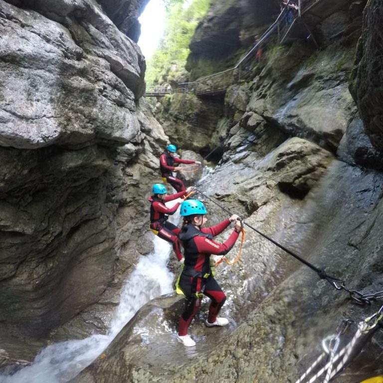 Drei Personen in Neoprenanzügen steigen in einer Felsenschlucht mit Wasser. Canyoning Starzlachklamm