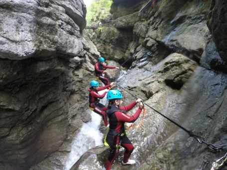 Drei Personen beim Canyoning in deiner Nähe in Neoprenanzügen klettern durch eine enge Schlucht mit Wasser.