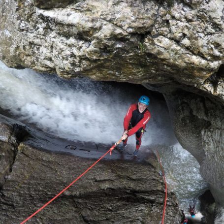 Person klettert in der Starzlachklamm an einem Felsen, gesichert mit einem Seil, über Wasserfall.