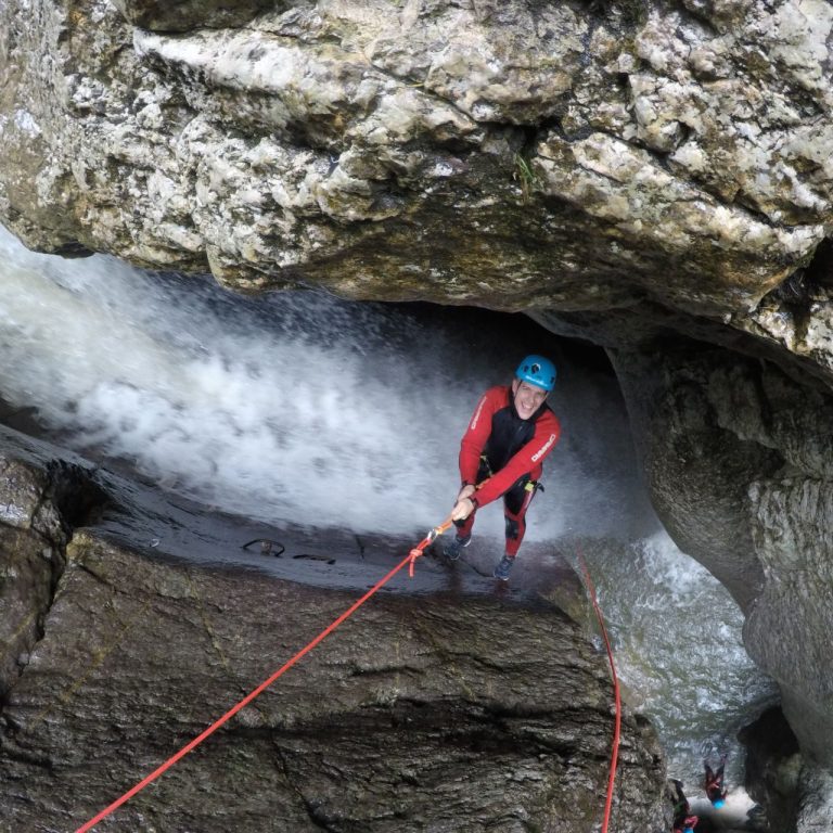 Eine Person klettert mit Seil in eine Höhle, umgeben von Wasser und Felsen in der Starzlachklamm