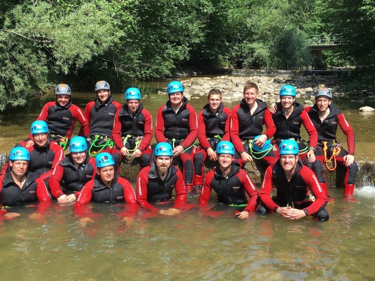 Junggesellenabschied in roten Anzügen und blauen Helmen im Wasser, bereit zum Canyoning in der Starzlachklamm