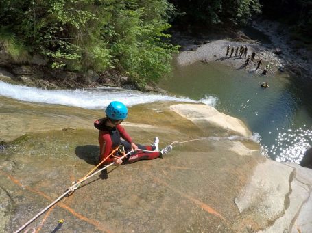 Person beim Canyoning in deiner Nähe sitzt am oberen Rand eines Wasserfalls und bereitet sich auf das Abseilen vor.